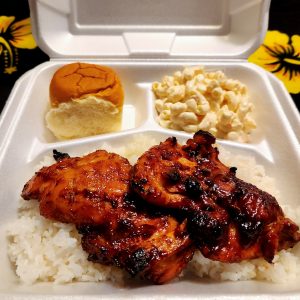 Disposable white 3 compartment container with a hinged lid, containing mac salad at 2 o'clock, white rice with Huli-Huli chicken over it at 3 o'clock to 9 o'clock, and Hawaiian sweet roll at 10 o'clock.
