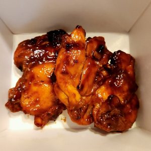 Up close image of Huli-Huli chicken contained in a white takeout box.