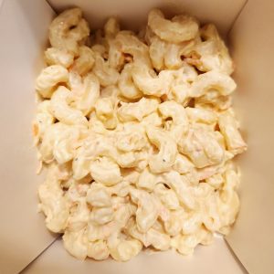 Up close image of mac salad contained in a white takeout box.