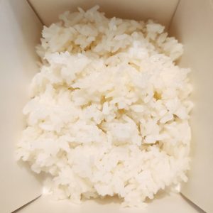 Up close image of white rice contained in a white takeout box.