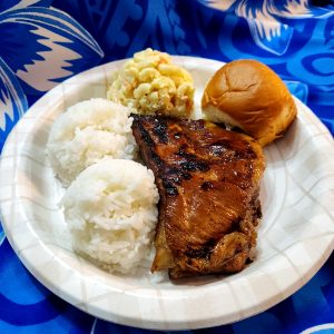 Disposable white plate, containing mac salad at 12 o'clock, Hawaiian sweet roll at 2 o'clock, sweet and sour pork spare ribs at 3 o'clock to 9 o'clock, and white rice at 6 o'clock to 9 o'clock.