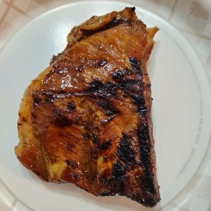 Up close image of sweet and sour spare ribs in the center of a white disposable plate.
